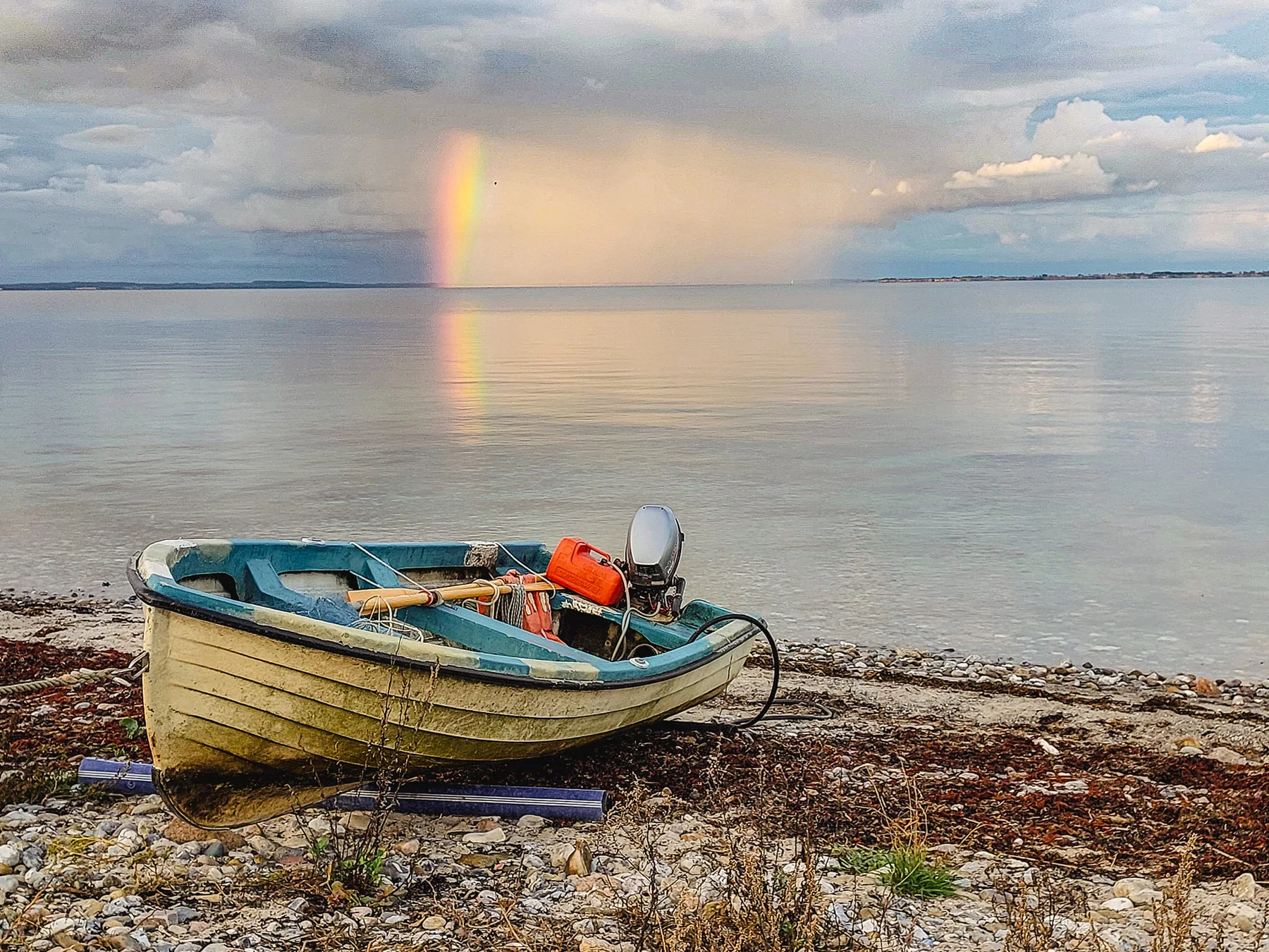 Kleines Boot am Ufer mit Regenbogen über dem Wasser